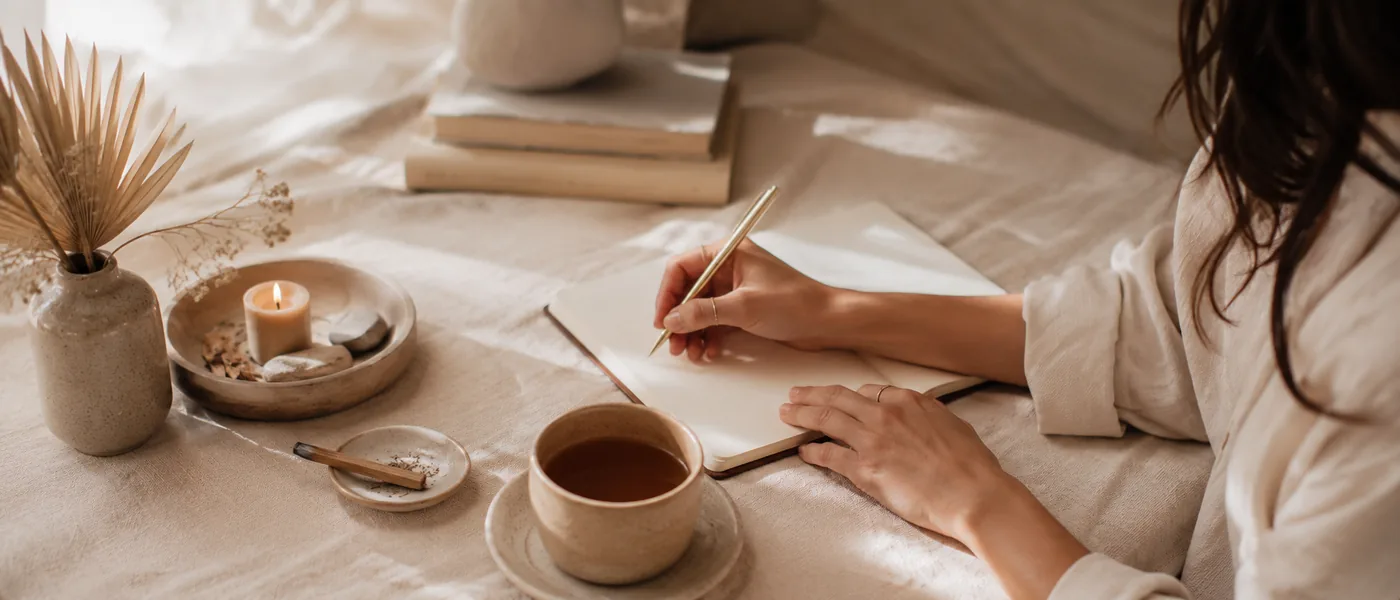 Manos escribiendo en un cuaderno junto a una taza de té